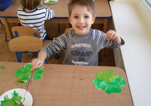 Widok na roześmianego chłopca, który maluje farbami sylwetę czterolistnej koniczynki.